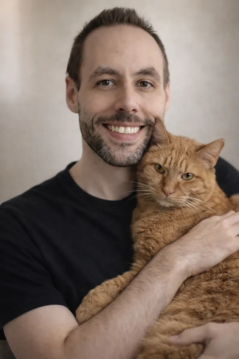 Patrick sitting with Meeko, his orange tabby cat, on the porch steps — the bond that inspired Evermeadow